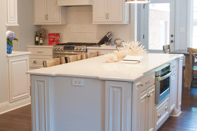 Imagen de cocina comedor tradicional con armarios con paneles con relieve, puertas de armario blancas, encimera de mármol, salpicadero blanco, salpicadero de azulejos tipo metro, electrodomésticos de acero inoxidable, suelo de madera en tonos medios y una isla