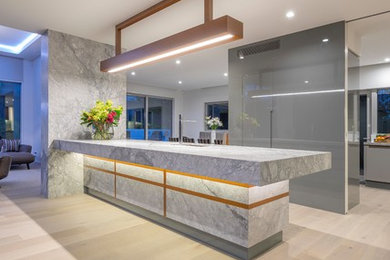 Photo of an expansive contemporary l-shaped kitchen/diner in Auckland with a submerged sink, flat-panel cabinets, grey cabinets, granite worktops, black appliances, light hardwood flooring, an island, beige floors and multicoloured worktops.