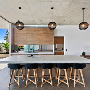 Contemporary galley open plan kitchen in Sunshine Coast with an integrated sink, flat-panel cabinets, medium wood cabinets, window splashback, stainless steel appliances, concrete floors, with island, brown floor and white benchtop.