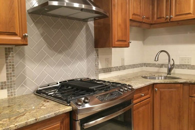 Elegant l-shaped kitchen photo in Newark with a drop-in sink, raised-panel cabinets, light wood cabinets, granite countertops, multicolored backsplash, ceramic backsplash, stainless steel appliances and an island