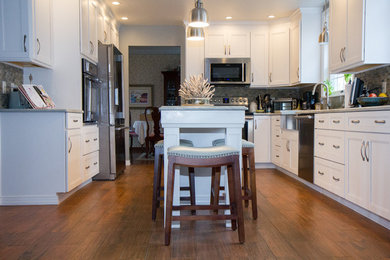 Example of a mid-sized transitional l-shaped medium tone wood floor and brown floor eat-in kitchen design in Other with a farmhouse sink, shaker cabinets, white cabinets, quartzite countertops, subway tile backsplash, stainless steel appliances and an island