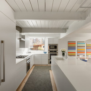 Idee per una cucina moderna con ante lisce, ante bianche, top in superficie solida, paraspruzzi bianco, elettrodomestici in acciaio inossidabile, parquet chiaro, isola e lavello integrato