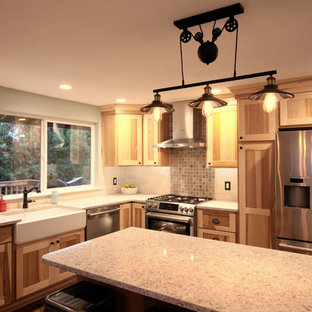 This is an example of a mid-sized country l-shaped eat-in kitchen in Seattle with a farmhouse sink, shaker cabinets, light wood cabinets, quartz benchtops, beige splashback, stone tile splashback, stainless steel appliances, medium hardwood floors, with island and brown floor.