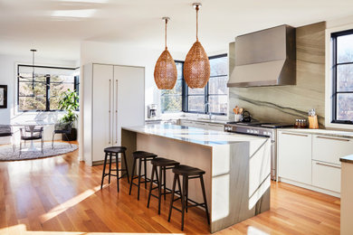 Bild på ett funkis grå grått kök, med vita skåp, grått stänkskydd, integrerade vitvaror, ljust trägolv, en köksö, en undermonterad diskho, släta luckor och stänkskydd i sten