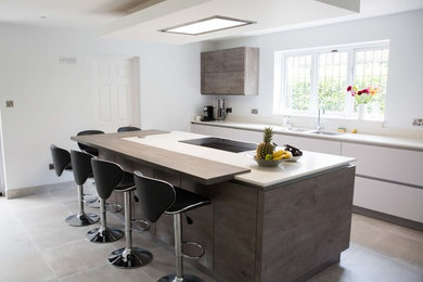 Inspiration for a medium sized modern open plan kitchen in Dorset with a submerged sink, flat-panel cabinets, white cabinets, quartz worktops, stainless steel appliances, ceramic flooring, an island and grey floors.