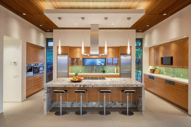 Enclosed kitchen - mid-sized tropical single-wall porcelain tile and beige floor enclosed kitchen idea in Hawaii with flat-panel cabinets, medium tone wood cabinets, green backsplash, glass tile backsplash, an island, an undermount sink, granite countertops and stainless steel appliances