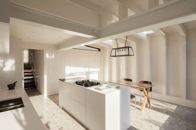 Photo of a medium sized contemporary galley open plan kitchen in London with an integrated sink, flat-panel cabinets, white cabinets, engineered stone countertops, white splashback, porcelain splashback, stainless steel appliances, terrazzo flooring and an island.