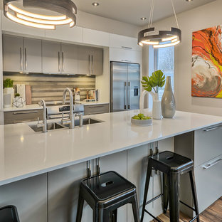 Photo of a mid-sized contemporary galley eat-in kitchen in Montreal with an undermount sink, flat-panel cabinets, grey cabinets, quartz benchtops, grey splashback, ceramic splashback, stainless steel appliances, cork floors, with island and grey floor.