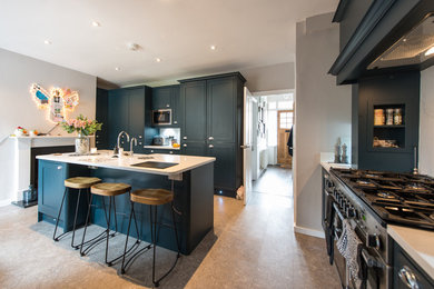Medium sized traditional l-shaped open plan kitchen in London with a belfast sink, shaker cabinets, blue cabinets, quartz worktops, white splashback, stainless steel appliances, an island and white worktops.