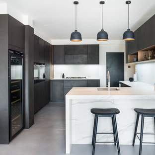 This is an example of a medium sized contemporary u-shaped kitchen in London with a submerged sink, flat-panel cabinets, black cabinets, concrete flooring, a breakfast bar, grey floors and white worktops.