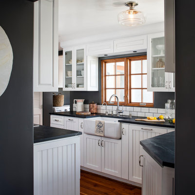 Mid-sized beach style u-shaped dark wood floor enclosed kitchen photo in San Francisco with a farmhouse sink, recessed-panel cabinets, white cabinets, soapstone countertops, white backsplash, subway tile backsplash, no island and stainless steel appliances