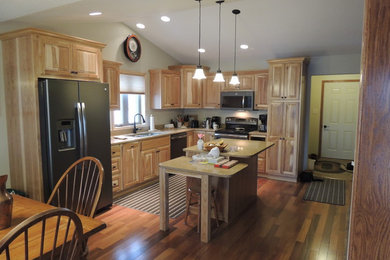 Mid-sized elegant l-shaped medium tone wood floor enclosed kitchen photo in Cedar Rapids with a double-bowl sink, raised-panel cabinets, medium tone wood cabinets, granite countertops, black appliances and an island