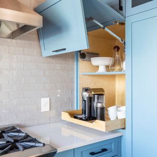 This is an example of a medium sized farmhouse u-shaped enclosed kitchen in Seattle with a belfast sink, shaker cabinets, blue cabinets, engineered stone countertops, white splashback, metro tiled splashback, stainless steel appliances, porcelain flooring, a breakfast bar, grey floors and white worktops.