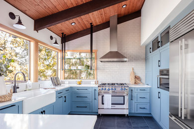 Kitchen - mid-sized cottage u-shaped gray floor and porcelain tile kitchen idea in Seattle with a farmhouse sink, shaker cabinets, blue cabinets, stainless steel appliances, white countertops, white backsplash, a peninsula, quartz countertops and subway tile backsplash