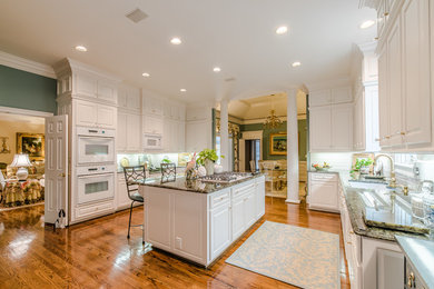 Huge elegant galley light wood floor open concept kitchen photo in Other with a double-bowl sink, raised-panel cabinets, white cabinets, quartzite countertops, white backsplash, subway tile backsplash, white appliances and an island