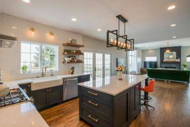 Example of a large transitional u-shaped medium tone wood floor and brown floor open concept kitchen design in Cedar Rapids with a farmhouse sink, shaker cabinets, blue cabinets, white backsplash, subway tile backsplash, stainless steel appliances, an island and white countertops
