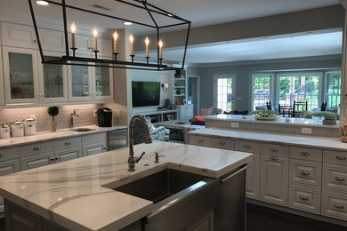 Example of a large transitional u-shaped brown floor and dark wood floor open concept kitchen design in St Louis with a farmhouse sink, white cabinets, gray backsplash, ceramic backsplash, stainless steel appliances, an island, raised-panel cabinets, quartzite countertops and white countertops