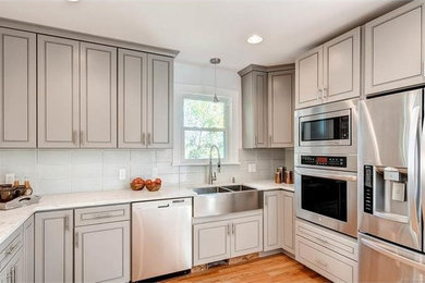 Eat-in kitchen - mid-sized craftsman u-shaped light wood floor and brown floor eat-in kitchen idea in Denver with a farmhouse sink, shaker cabinets, gray cabinets, quartz countertops, white backsplash, glass tile backsplash, stainless steel appliances and a peninsula