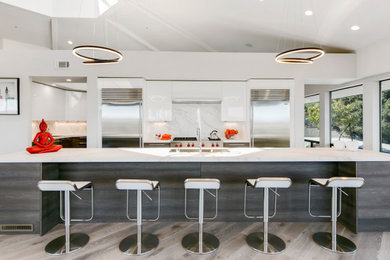 Example of a large trendy galley light wood floor and gray floor open concept kitchen design in San Francisco with an undermount sink, flat-panel cabinets, gray cabinets, quartz countertops, white backsplash, stainless steel appliances, an island and white countertops