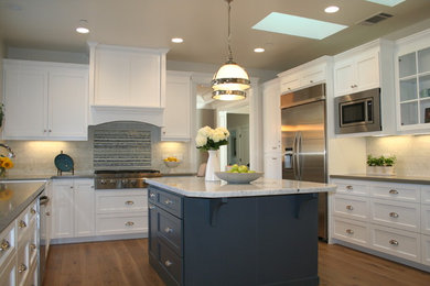 Example of a mid-sized classic u-shaped medium tone wood floor enclosed kitchen design in San Francisco with a farmhouse sink, white cabinets, quartzite countertops, beige backsplash, stainless steel appliances, an island, shaker cabinets and stone tile backsplash