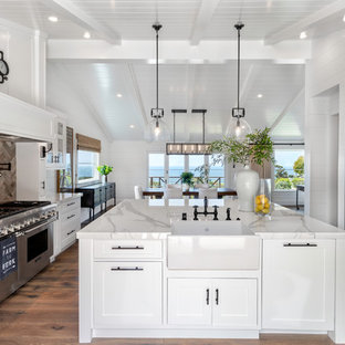 Inspiration for a mid-sized country u-shaped eat-in kitchen in Orange County with a farmhouse sink, shaker cabinets, white cabinets, stainless steel appliances, medium hardwood floors, with island, brown floor, white benchtop, marble benchtops, white splashback and timber splashback.