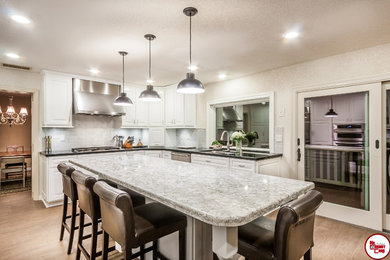 Example of a large classic u-shaped light wood floor enclosed kitchen design in Orange County with an undermount sink, raised-panel cabinets, white cabinets, quartz countertops, white backsplash, glass tile backsplash, stainless steel appliances and an island
