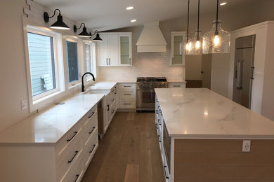 Example of a mid-sized transitional u-shaped medium tone wood floor and brown floor open concept kitchen design in Calgary with a farmhouse sink, shaker cabinets, white cabinets, quartzite countertops, white backsplash, subway tile backsplash, stainless steel appliances, an island and white countertops