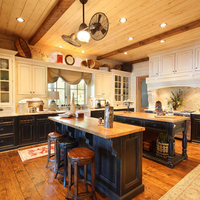 Enclosed kitchen - rustic l-shaped medium tone wood floor and brown floor enclosed kitchen idea in Atlanta with recessed-panel cabinets, wood countertops, beige backsplash, stone tile backsplash, a farmhouse sink, stainless steel appliances, two islands and beige countertops