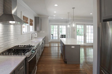 Inspiration for a medium tone wood floor and brown floor kitchen remodel in Atlanta with a farmhouse sink, shaker cabinets, gray cabinets, quartz countertops, white backsplash, ceramic backsplash, stainless steel appliances, an island and white countertops