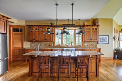 Example of a mid-sized arts and crafts l-shaped light wood floor eat-in kitchen design in New York with a farmhouse sink, recessed-panel cabinets, medium tone wood cabinets, granite countertops, beige backsplash, stone tile backsplash, stainless steel appliances and an island