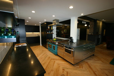 Foto på ett mellanstort funkis kök, med en dubbel diskho, släta luckor, svarta skåp, bänkskiva i betong, vitt stänkskydd, stänkskydd i tunnelbanekakel, rostfria vitvaror, ljust trägolv, en halv köksö och brunt golv