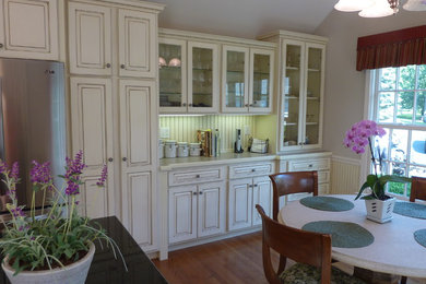 Exemple d'une cuisine américaine chic en L avec un placard avec porte à panneau surélevé, des portes de placard blanches, un plan de travail en bois et une crédence blanche.