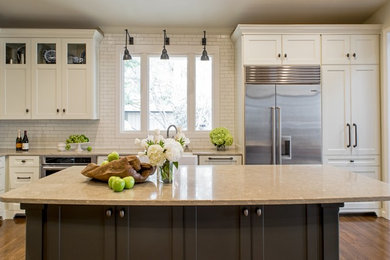 Elegant l-shaped medium tone wood floor open concept kitchen photo in Austin with a farmhouse sink, recessed-panel cabinets, white cabinets, limestone countertops, white backsplash, subway tile backsplash, stainless steel appliances and an island