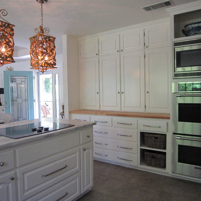 Eclectic l-shaped porcelain tile open concept kitchen photo in Dallas with a farmhouse sink, raised-panel cabinets, white cabinets, wood countertops, stainless steel appliances and an island