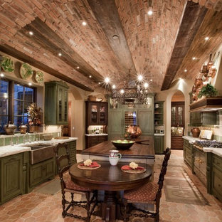 Large mediterranean u-shaped eat-in kitchen in Las Vegas with a farmhouse sink, raised-panel cabinets, green cabinets, with island, wood benchtops, green splashback, stone tile splashback, stainless steel appliances and terra-cotta floors.