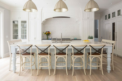 Mid-sized beach style l-shaped brown floor and light wood floor eat-in kitchen photo in Minneapolis with an undermount sink, recessed-panel cabinets, white cabinets, white backsplash, an island, marble countertops, marble backsplash and stainless steel appliances