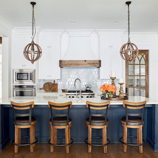 Idee per un cucina con isola centrale stile marino con ante in stile shaker, ante bianche, paraspruzzi bianco, elettrodomestici in acciaio inossidabile, parquet scuro e top bianco