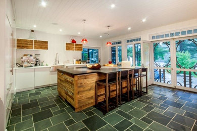Mid-sized mountain style single-wall slate floor and green floor enclosed kitchen photo in Other with a farmhouse sink, flat-panel cabinets, distressed cabinets, quartz countertops, white backsplash, wood backsplash, stainless steel appliances and an island