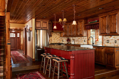 Inspiration for a medium sized rustic l-shaped kitchen in Minneapolis with a belfast sink, raised-panel cabinets, medium wood cabinets, granite worktops, stainless steel appliances, dark hardwood flooring, an island, brown floors and multi-coloured splashback.