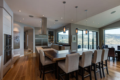 Moderne Wohnküche mit integriertem Waschbecken, Granit-Arbeitsplatte, Küchenrückwand in Blau, Rückwand aus Glasfliesen, Küchengeräten aus Edelstahl, braunem Holzboden und Kücheninsel in Vancouver