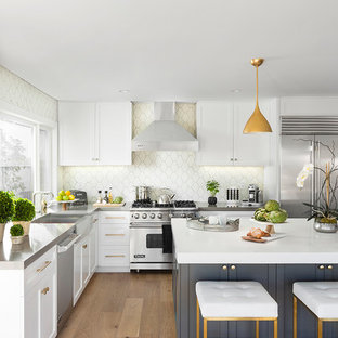 Example of a mid-sized transitional l-shaped light wood floor and beige floor eat-in kitchen design in Los Angeles with white cabinets, stainless steel appliances, an island, a farmhouse sink, recessed-panel cabinets and beige backsplash