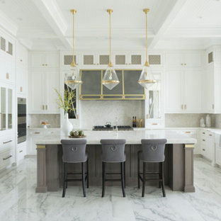 This is an example of an expansive transitional u-shaped eat-in kitchen in Chicago with a farmhouse sink, recessed-panel cabinets, white cabinets, quartzite benchtops, white splashback, stone slab splashback, panelled appliances, marble floors, with island, white floor and white benchtop.