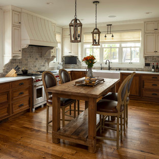 Mid-sized rustic eat-in kitchen pictures - Example of a mid-sized mountain style l-shaped dark wood floor and brown floor eat-in kitchen design in Minneapolis with a farmhouse sink, beaded inset cabinets, distressed cabinets, brown backsplash, brick backsplash, an island, white countertops and paneled appliances
