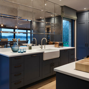 Contemporary kitchen in Gloucestershire with shaker cabinets, blue cabinets, metallic splashback, mirror splashback, light hardwood flooring, beige floors and white worktops.