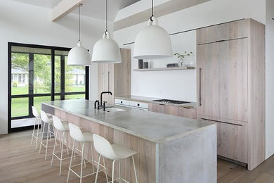 Inspiration for a mid-sized modern single-wall medium tone wood floor and brown floor open concept kitchen remodel in Other with an island, an undermount sink, flat-panel cabinets, light wood cabinets, concrete countertops, paneled appliances and gray countertops