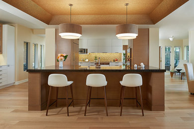 Example of a large transitional u-shaped light wood floor, beige floor and tray ceiling eat-in kitchen design with flat-panel cabinets, beige backsplash, paneled appliances, an island, an undermount sink, mosaic tile backsplash, black countertops and medium tone wood cabinets