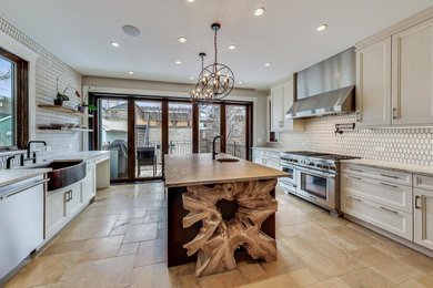 Example of a large transitional galley travertine floor and beige floor enclosed kitchen design with a farmhouse sink, recessed-panel cabinets, white cabinets, marble countertops, stainless steel appliances and an island