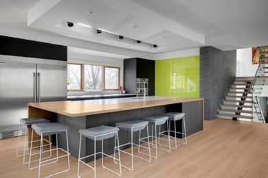 Mid-sized trendy l-shaped vinyl floor and beige floor eat-in kitchen photo in Calgary with an undermount sink, flat-panel cabinets, granite countertops, gray backsplash, stone slab backsplash, stainless steel appliances, an island, gray countertops and green cabinets