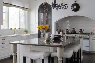 Пример оригинального дизайна: п-образная кухня среднего размера в классическом стиле с с полувстраиваемой мойкой (с передним бортиком), белым фартуком, фартуком из плитки кабанчик, белой техникой, обеденным столом, фасадами с выступающей филенкой, белыми фасадами, темным паркетным полом, островом, коричневым полом и белой столешницей