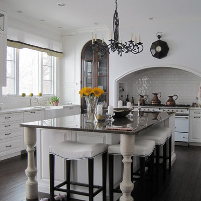 Mid-sized elegant u-shaped dark wood floor and brown floor eat-in kitchen photo in Detroit with a farmhouse sink, white backsplash, subway tile backsplash, white appliances, raised-panel cabinets, white cabinets, an island and white countertops
